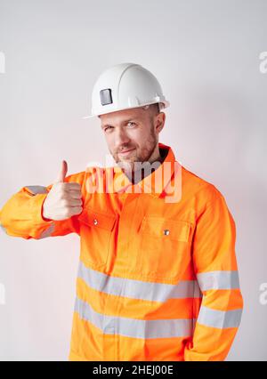 Niedlicher kaukasischer Cheftechniker, Supervisor oder Bauarchitekt mit Bart, Arbeitsuniform und Hardhut, der eine Geste mit Daumen nach oben macht. Konzept der Bauindustrie. Hochwertige Fotos Stockfoto
