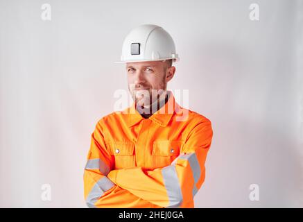 Lächelnder junger Bauarbeiter oder Techniker mit Schutzhelm. Bärtiger männlicher Supervisor oder Bauarchitekt in weißem Schutzhut und orangefarbener Warnweste. Hochwertige Fotos Stockfoto