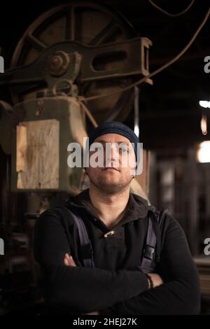 Porträt eines jungen männlichen Zimmermanns, eines jungen männlichen Zimmermanns, der in seinem Laden steht Stockfoto