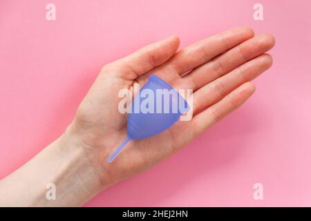 Junge Frau Handfläche hält zeitgenössische lila Silikon Menstruationstasse auf rosa Farbe Hintergrund extreme Nahsicht von oben Stockfoto