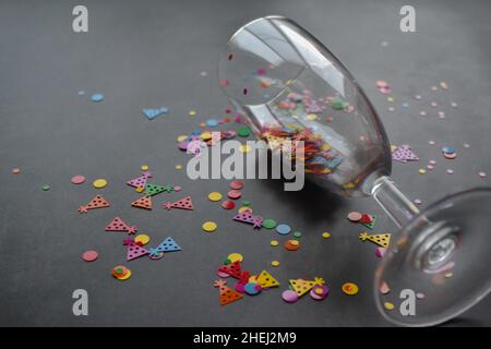 Ein Weinglas mit Spritzern Konfetti auf dunklem Hintergrund. Speicherplatz kopieren. Konzept von Party, Feier, Neujahr, Weihnachten, Geburtstag Stockfoto