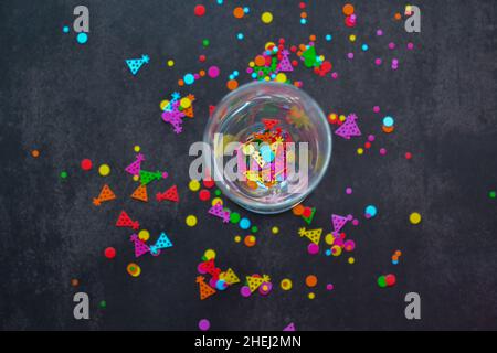 Ein Weinglas mit Spritzern Konfetti auf dunklem Hintergrund. Speicherplatz kopieren. Konzept von Party, Feier, Neujahr, Weihnachten, Geburtstag Stockfoto