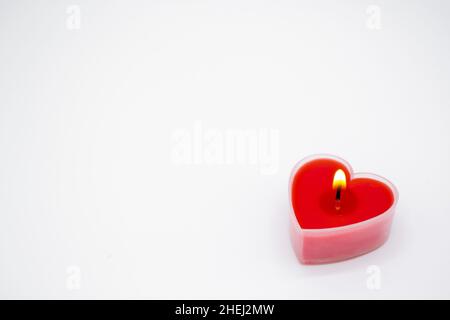 Eine rote herzförmige Kerze brennt auf weißem Hintergrund. Speicherplatz kopieren. Konzept der Liebe, Valentinstag, Leidenschaft. Stockfoto