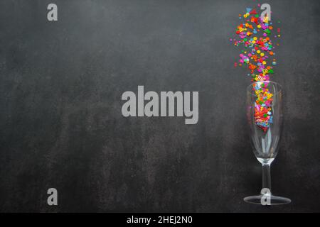 Ein Weinglas mit Spritzern Konfetti auf dunklem Hintergrund. Speicherplatz kopieren. Konzept von Party, Feier, Neujahr, Weihnachten, Geburtstag Stockfoto