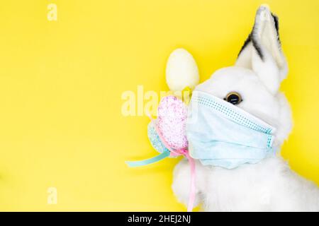 Osterhase in einer medizinischen Gesichtsmaske mit einem Bouquet aus bunten Eiern. Das Konzept von Ostern und Quarantäne während des Coronavirus. Wie ein Postkartenmotiv Stockfoto