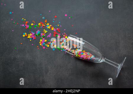 Ein Weinglas mit Spritzern Konfetti auf dunklem Hintergrund. Speicherplatz kopieren. Konzept von Party, Feier, Neujahr, Weihnachten, Geburtstag Stockfoto