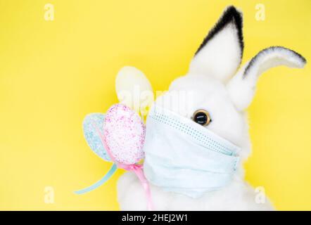 Osterhase in einer medizinischen Gesichtsmaske mit einem Bouquet aus bunten Eiern. Das Konzept von Ostern und Quarantäne während des Coronavirus. Wie ein Postkartenmotiv Stockfoto