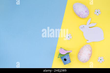 Osterlack: Osterhase, Blumen, Vogelhaus mit Vogel und bunte Eier auf gelbem Hintergrund, Platz für Text auf blauem Hintergrund. Stockfoto