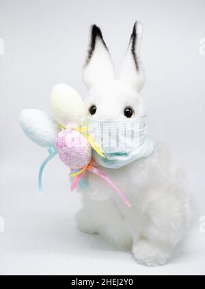 Osterhase in einer medizinischen Gesichtsmaske mit einem Bouquet aus bunten Eiern. Das Konzept von Ostern und Quarantäne während des Coronavirus. Wie ein Postkartenmotiv Stockfoto