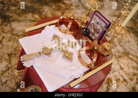 Kreuz, goldene Kronen und Kerzenständer stehen auf dem Tisch in der Kirche. Draufsicht Stockfoto