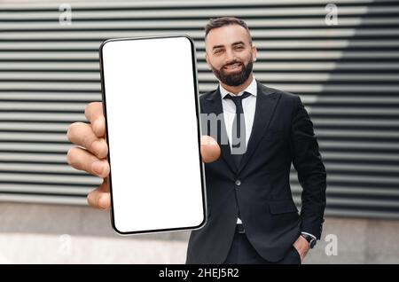 Lächelnder Männlicher Unternehmer Im Anzug Hält Großes Smartphone Mit Leerem Weißen Bildschirm Stockfoto