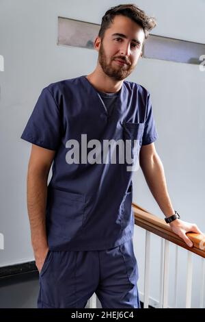 Junger lächelnder junger männlicher Arzt Zahnarzt in dunkelblauer Uniform, der im Flur steht. Stockfoto