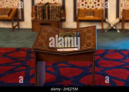 AMMAN, JORDANIEN - 27. SEPTEMBER 2021: Heiliger Koran mit Al-Quran Al Kareem Islamische Kalligraphie auf einem Bücherstand im Gebetsraum der Moschee des Königs Stockfoto