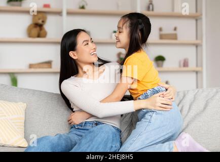 Glücklich zufrieden chinesischen jungen weiblichen Blick auf Mädchen haben Spaß, Umarmung, genießen Zeit zusammen im Wohnzimmer Stockfoto