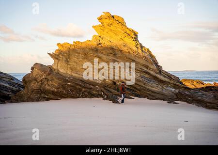 Porto Covo, Portugal - 4. November 2021: Ein Fischer mit Angelausrüstung zu Fuß am Strand mit schönen Felsformationen, Sines, Portugal Stockfoto