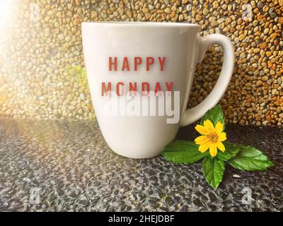 Happy monday Text auf Kaffeebecher mit gelber Blume und braunem Marmorhintergrund. Morgenkonzept. Stockfoto