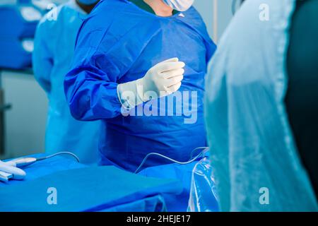 Ein Chirurg in weißen sterilen Handschuhen und einem blauen OP-Kittel im Operationssaal. Selektiver Fokus. Der Arzt ist bereit, mit der Operation zu beginnen. Stockfoto