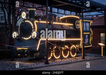 Zamek Topacz, Polen - 01. Januar 2022: Eine schwarze Oldtimer-Lokomotive, die mit Weihnachtslichtern mit LED-Beleuchtung geschmückt ist. Stockfoto