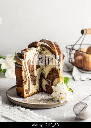 Osterkomposition mit in Scheiben geschnittenem Marmorkuchen, Blumen und Eiern auf hellem Hintergrund Stockfoto