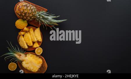 In Scheiben geschnittene Ananas in verschiedenen Formen. Reife Ananas auf Schneidebrett Kochen Sommer Dessert auf schwarzem Hintergrund. Flach liegend. Langes Webbanner mit Kopie Stockfoto