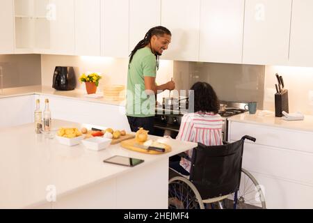 afroamerikanische behinderte Frau im Rollstuhl und Ehemann, der in der Küche kocht Stockfoto