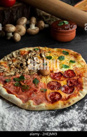 Italienische Pizza Four Seasons (Pizza Quattro Stagioni) mit verschiedenen Zutaten auf dem Holztisch in der Küche. Hausgemachte italienische Rezepte Stockfoto