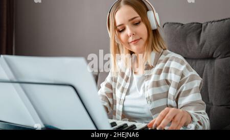 Frau in Kopfhörern, die Klaviermusik auf Synthesizer aus Noten spielt. Teenager Mädchen Musiker Pianist verbessert Fähigkeiten spielen Klavier. Langes Webbanner Stockfoto