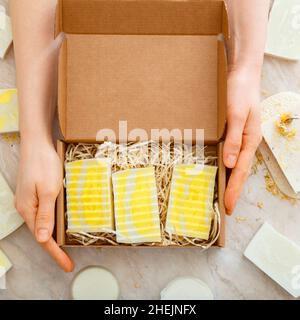 Geschenkbox mit Naturseife in weiblichen Händen. DIY Seifen-Set. Viele verschiedene hausgemachte Barseifen. Hygieneartikel Flat Lay Long Square Nahaufnahme. Stockfoto