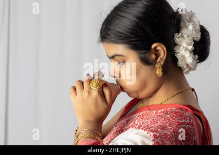 Eine schöne indische Frau in rot Saree weht Muschel auf weißem Hintergrund Stockfoto