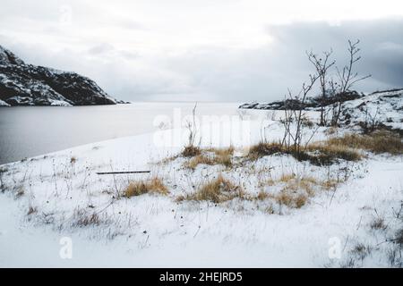 Winterhimmel über der schneebedeckten Küste entlang des gefrorenen Fjords, Nusfjord, Nordland County, Lofoten Islands, Norwegen Stockfoto