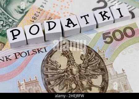 Die Formulierung „Podatki“ wurde mit „Steuern“ und vielen polnischen Banknoten übersetzt. Neue Steuervorschriften in Polen ab 2022. Foto aufgenommen unter künstlichem, weichem Licht Stockfoto