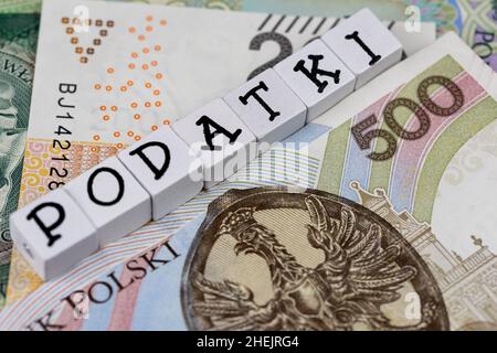 Die Formulierung „Podatki“ wurde mit „Steuern“ und vielen polnischen Banknoten übersetzt. Neue Steuervorschriften in Polen ab 2022. Foto aufgenommen unter künstlichem, weichem Licht Stockfoto