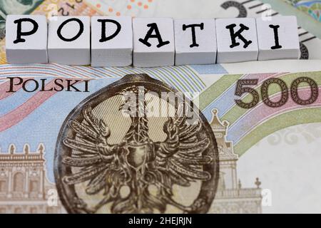Die Formulierung „Podatki“ wurde mit „Steuern“ und vielen polnischen Banknoten übersetzt. Neue Steuervorschriften in Polen ab 2022. Foto aufgenommen unter künstlichem, weichem Licht Stockfoto