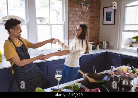 Fröhliches junges biracial Paar tanzen während der Zubereitung Mahlzeit zusammen in der Küche zu Hause Stockfoto