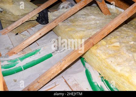 Erweiterte Perlit- und Mineralwollisolierung auf Rohren in der häuslichen Lüftung mit Wärmerückgewinnung verlegt, grüne Rohre auf dem Dachstuhl verlegt. Stockfoto