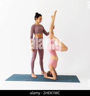 Eine Trainerin hilft einem Schüler, die Shirshasana-Übung, eine invertierte Asana, richtig durchzuführen, trainiert im Studio auf weißem Hintergrund Stockfoto