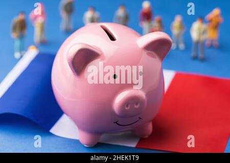 Sparschwein, französische Flagge und Plastikspielzeugmänner auf farbigem Hintergrund, Konzept zum Thema Einkommen der Bevölkerung Frankreichs Stockfoto