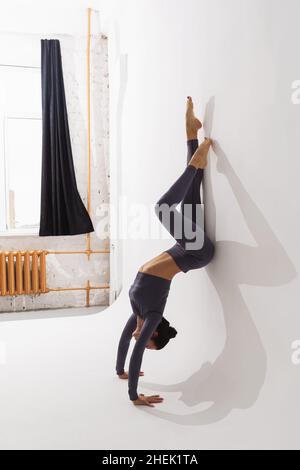 Eine Frau, die Yoga praktiziert, die Adho Mukha Vrikshasana-Übung macht, mit Füßen an der Wand, Handstand, invertiertem Asana Stockfoto