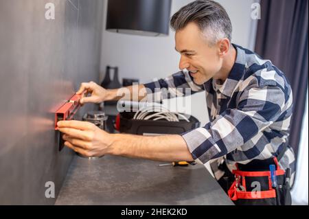 Mann, der das Messgerät an eine Wand in der Nähe der Steckdose anfasst Stockfoto