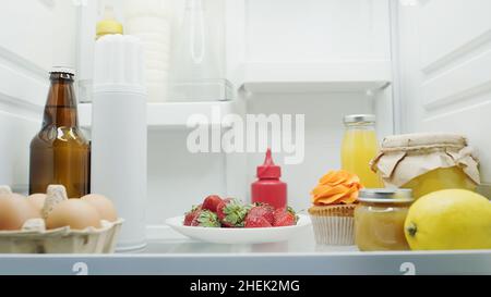 Bier, Eier, frische Erdbeeren, Zitrone, Cupcake, Orangensaft, Honig und Saucen im Kühlschrank Stockfoto