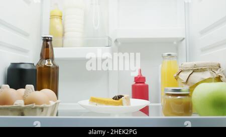 Leckere Kuchen, Eier, Apfel, Flaschen mit Getränken, Saucen, Honig- und Fruchtpüree im Kühlschrank Stockfoto