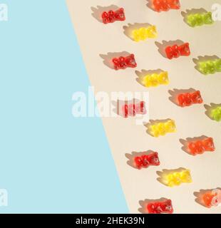 Kreatives Muster mit bunten Gummibären auf dem beigen und pastellblauen Hintergrund. Sommer flach liegend. Stockfoto