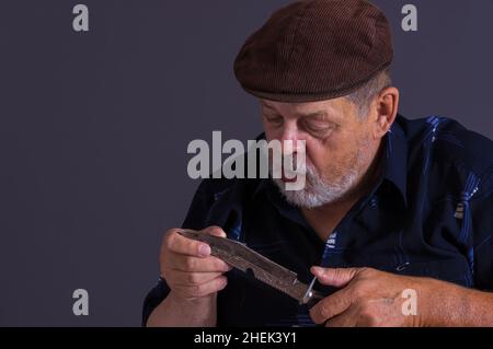 Bärtiger kaukasischer älterer Mann, der ein rostiges Messer hält und untersucht Stockfoto