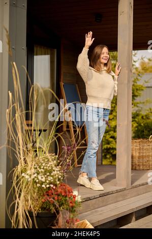 Frau, die auf der Veranda des Hauses steht, begrüßt sie Stockfoto
