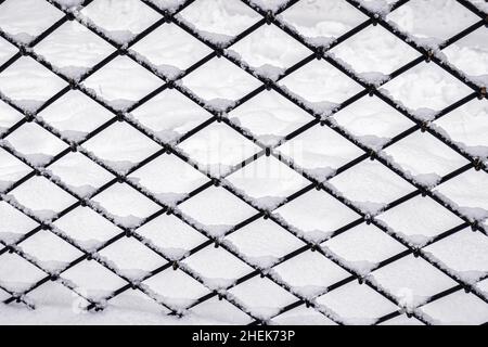 Schwarzes Metallgitter im Winter mit Schnee bedeckt. Schneefall- und Winterwetterkonzept. Stockfoto