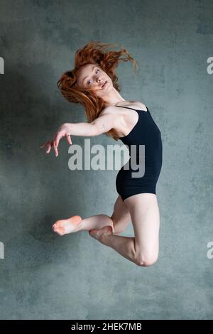 Petitie-Tänzerin mit fließendem rotbraunem Haar, die in schwarzen Shorts und Trikot im Fotostudio tanzt Stockfoto