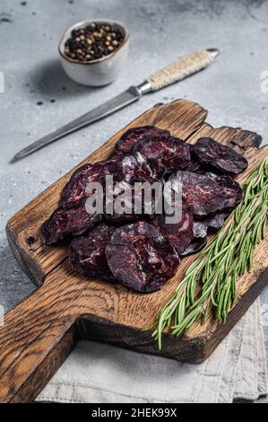 Geschnittene Pferdewurst auf Holzbrett mit Kräutern. Grauer Hintergrund. Draufsicht Stockfoto