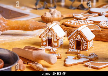 Weihnachts-Lebkuchenhäuser und verschieden geformte Kekse mit Zuckereier auf Holztisch, Nahaufnahme mit selektivem Fokus Stockfoto