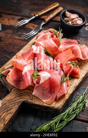 Scheiben Schinken aus Jamon serrano oder Prosciutto crudo parma auf Holzbrett mit Rosmarin. Holzhintergrund. Draufsicht Stockfoto