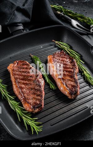 Gegrilltes Top-Lendenrindsteak oder brasilianisches Picanha, gebratenes Fleisch auf der Grillpfanne. Schwarzer Hintergrund. Draufsicht Stockfoto